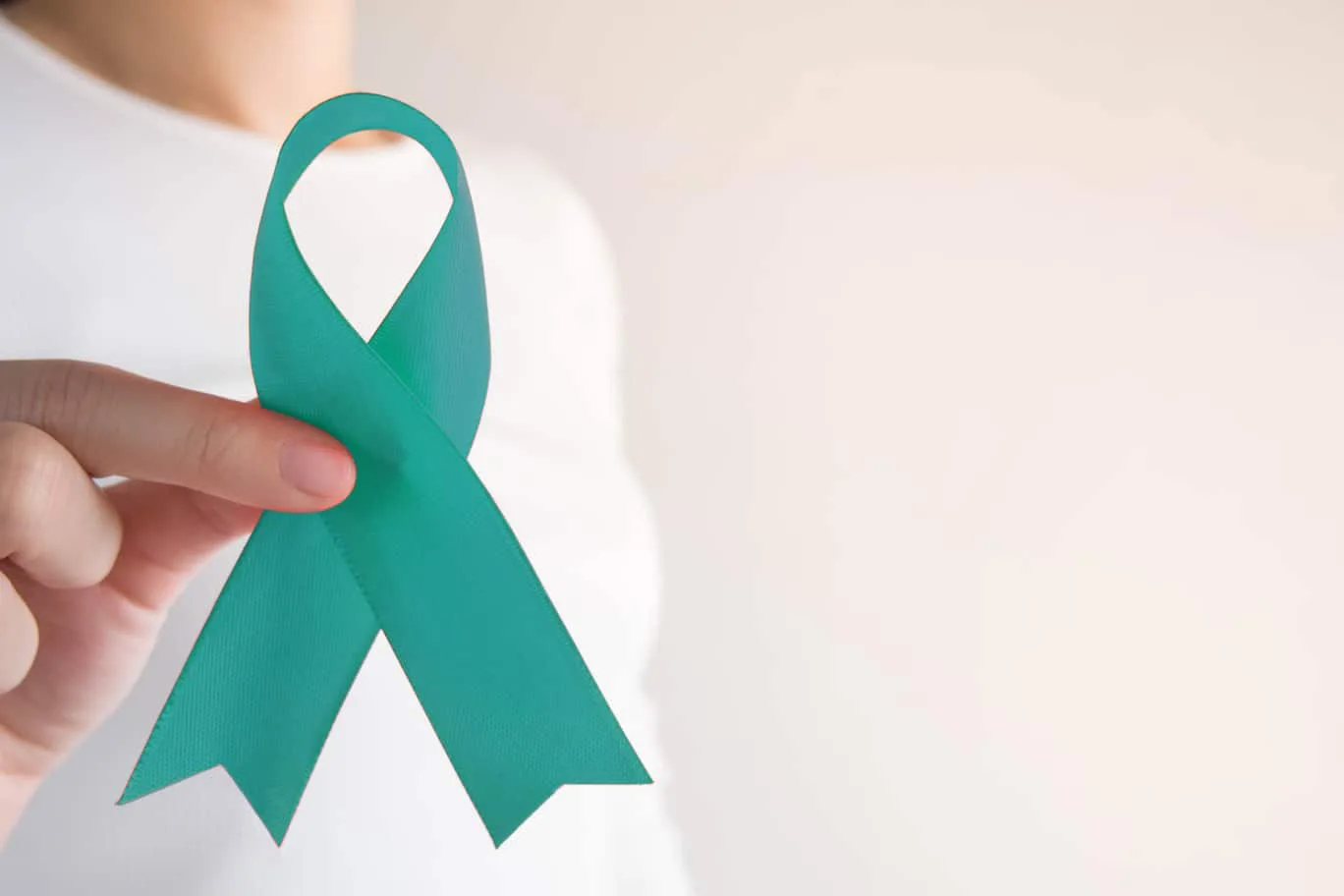 Close up of a woman’s hand holding a PCOS teal ribbon.