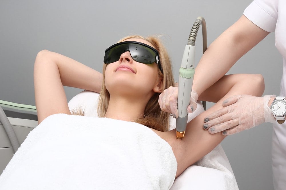 Image of woman laying on treatment bed while nurse performs laser hair removal on her armpit.